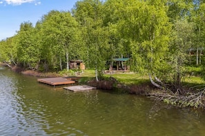 A riverside cabin with a dock, surrounded by lush greenery and trees.