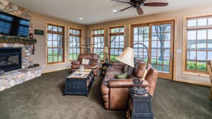 A spacious living room with a stone fireplace, leather sofas, and large windows offering a view of a lake. - Lake Miltona Family Vacation in the Alexandria Lakes area (Miltona)