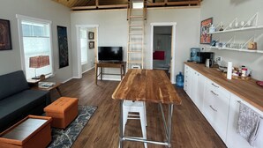 A compact living space with a loft area, a kitchen with white cabinets, a wooden dining table, and a television in the living area. - Clean, modern guesthouse located in a central Austin. (Austin)