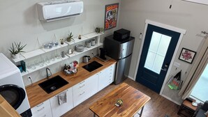 A compact kitchen with white cabinets, a wooden countertop, a stainless steel refrigerator, a microwave, and a dining table. - Clean, modern guesthouse located in a central Austin. (Austin)