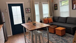 A cozy living area with a dark blue door, a wooden table with a bowl, a grey sofa with orange cushions, and a patterned rug. - Clean, modern guesthouse located in a central Austin. (Austin)