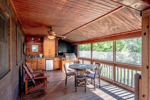 Une terrasse en bois avec un barbecue et un espace repas, des murs en bois et de grandes fenêtres.