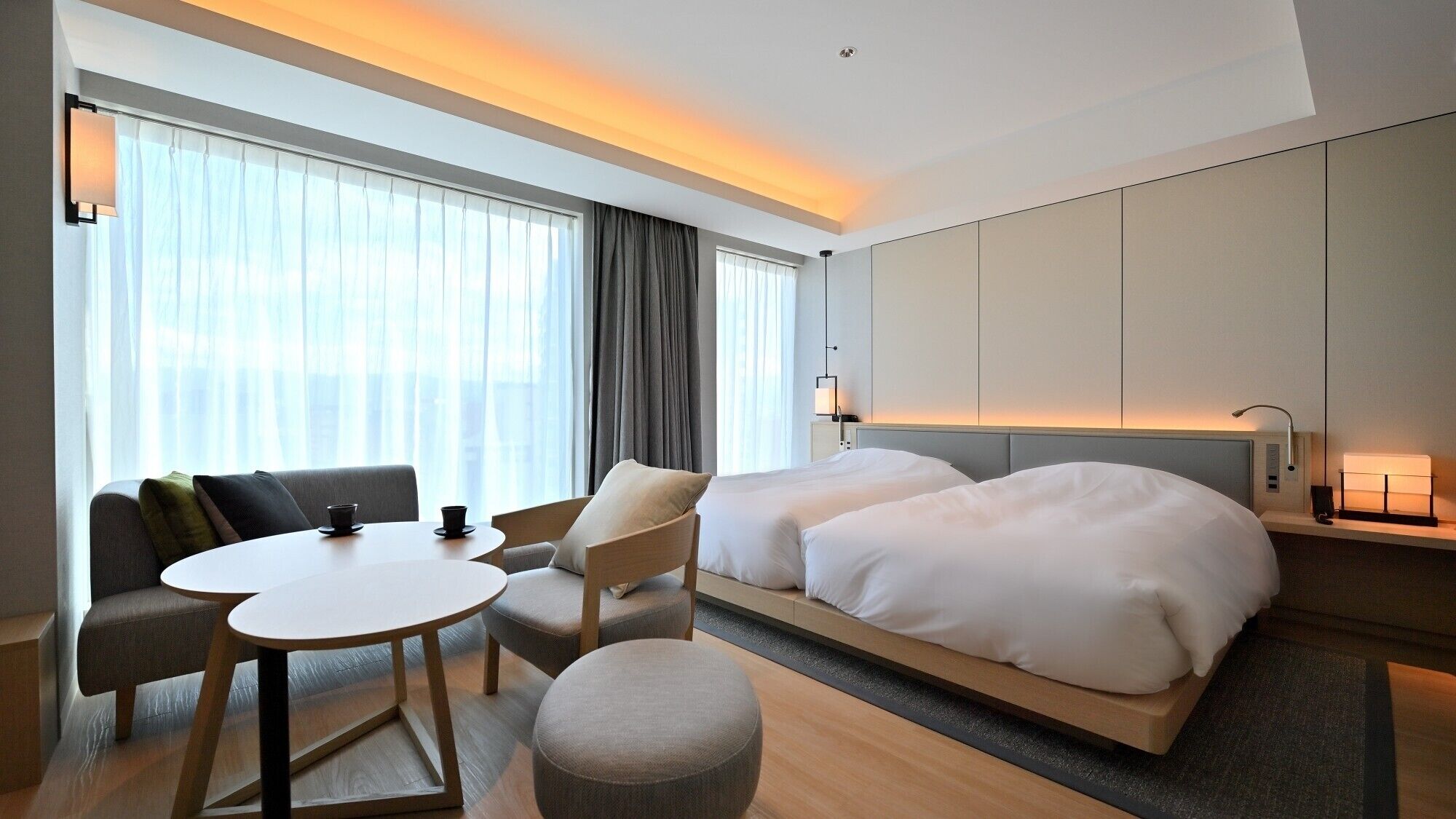 A hotel room with a bed, two bedside tables, a sofa, a round table, and a chair.