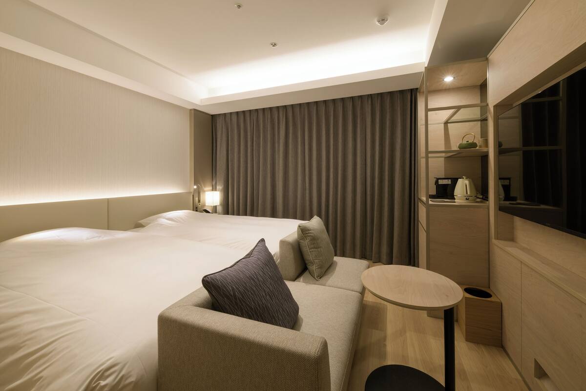 Une chambre d’hôtel moderne avec un grand lit, un canapé, une petite table ronde et un téléviseur encastré.