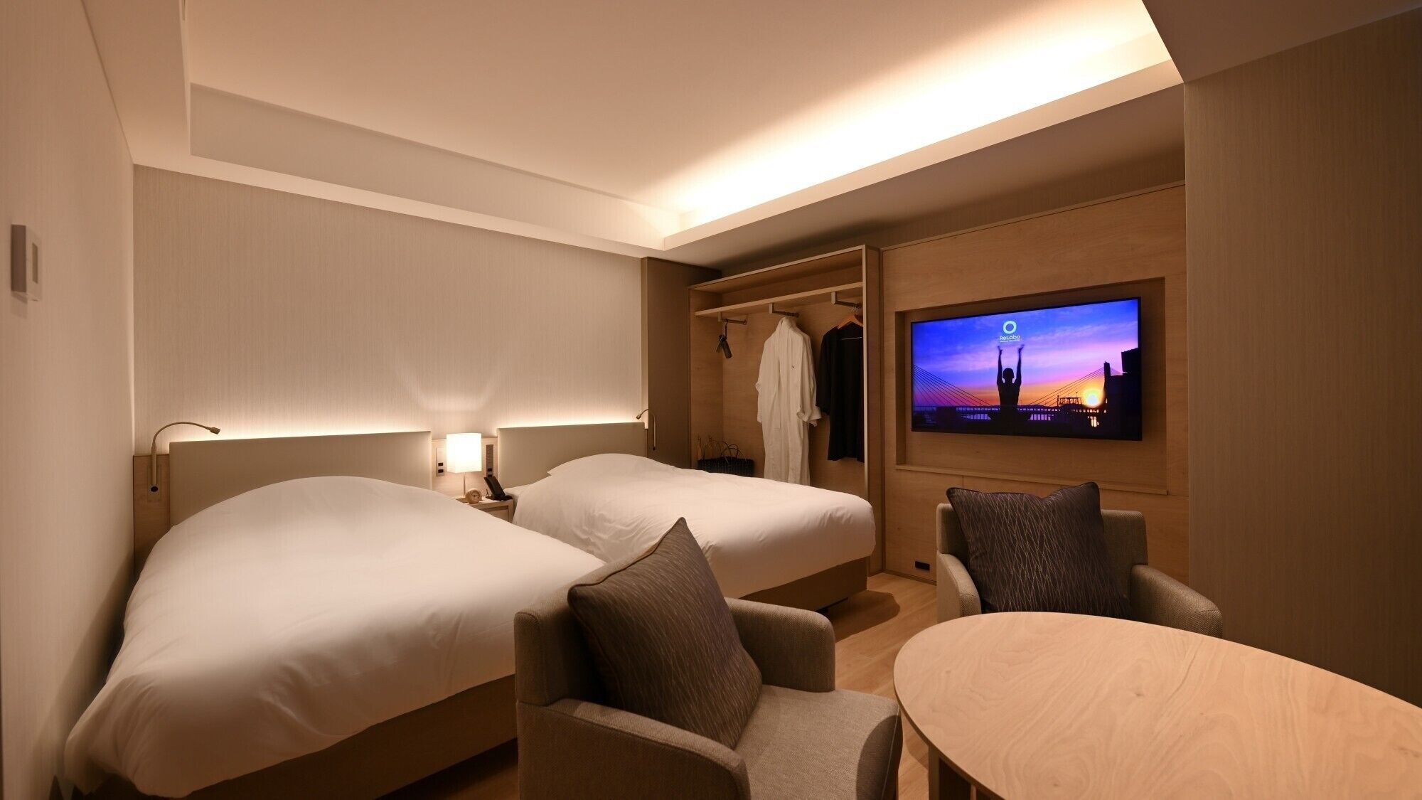 A hotel room with two beds, a TV, a seating area, and a wardrobe.