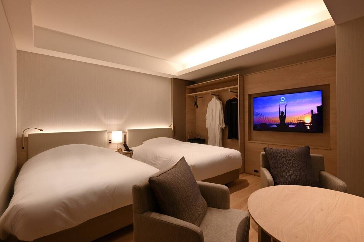 Une chambre d’hôtel avec deux lits, une télévision, un coin salon et une armoire.