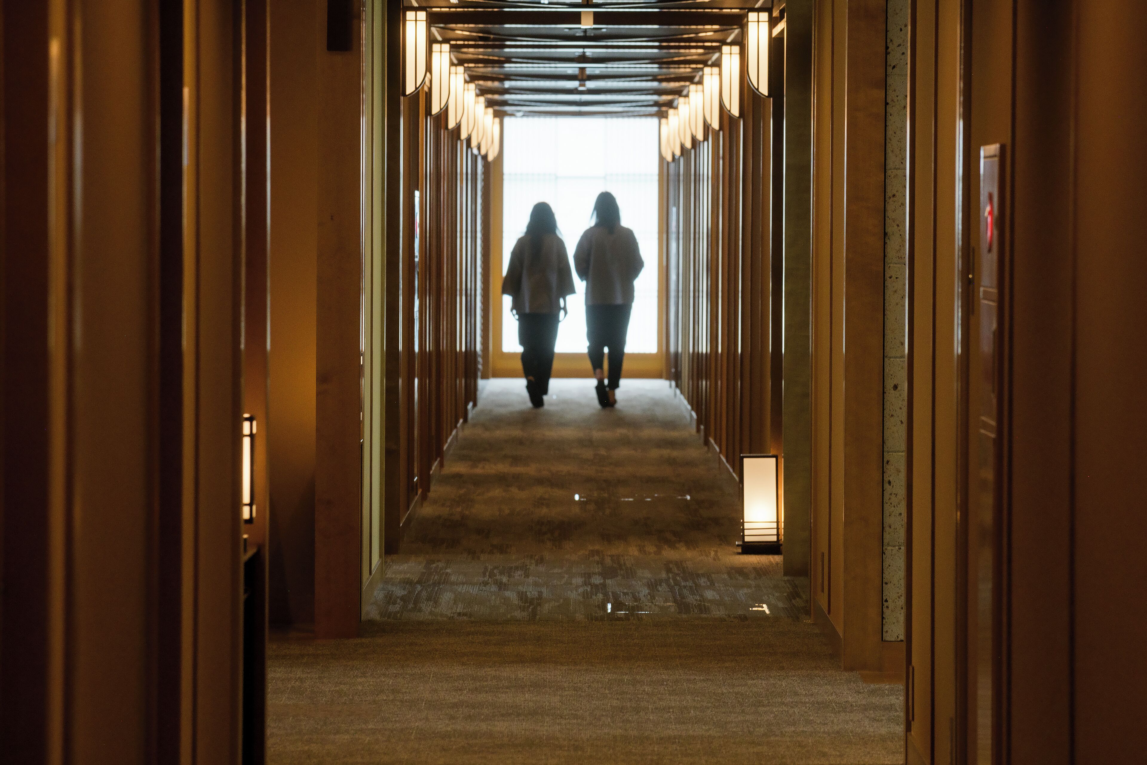 A corridor with a wooden floor and walls, leading to a bright exit.