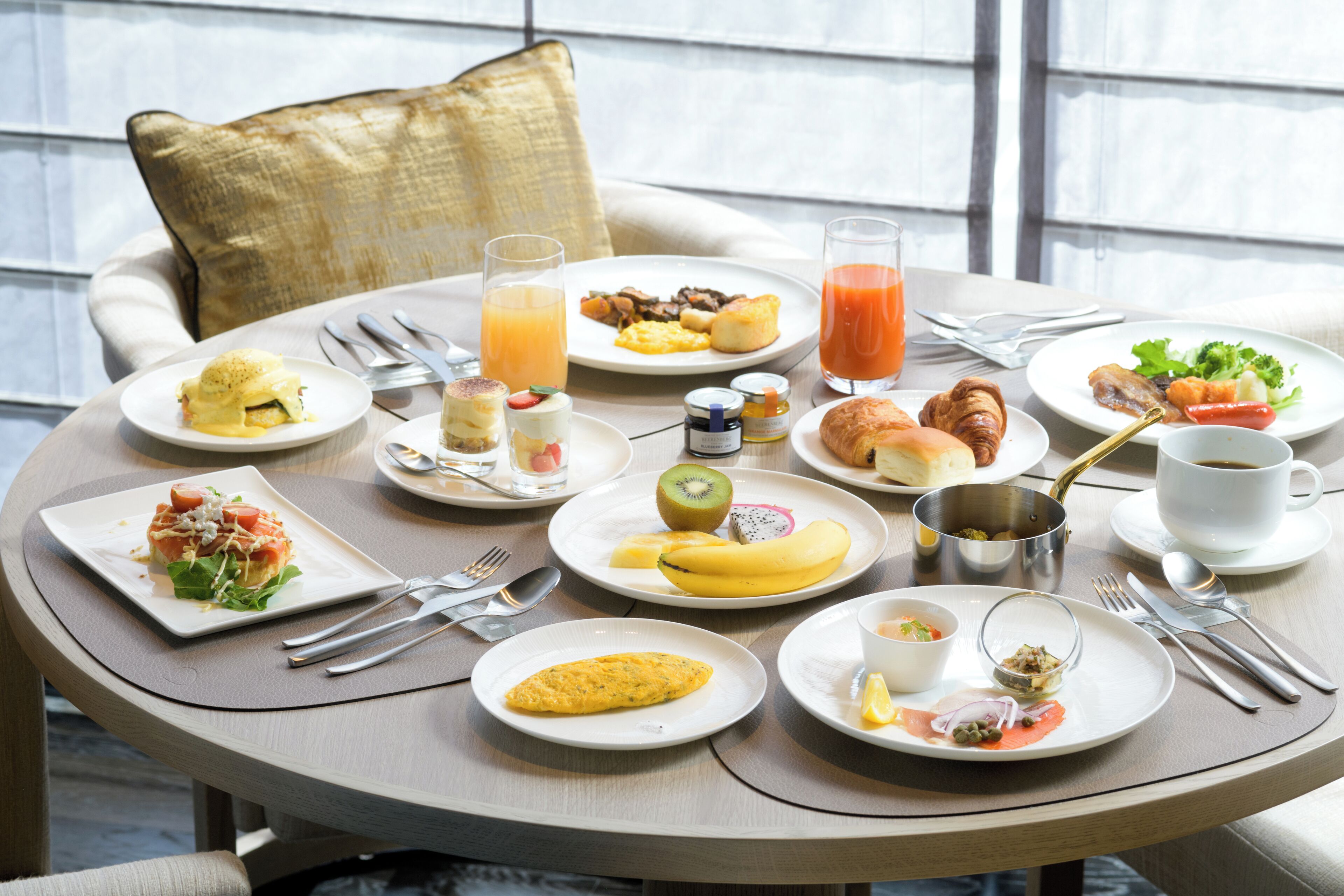 Uma mesa de café da manhã com diversos pratos, utensílios e uma bebida.