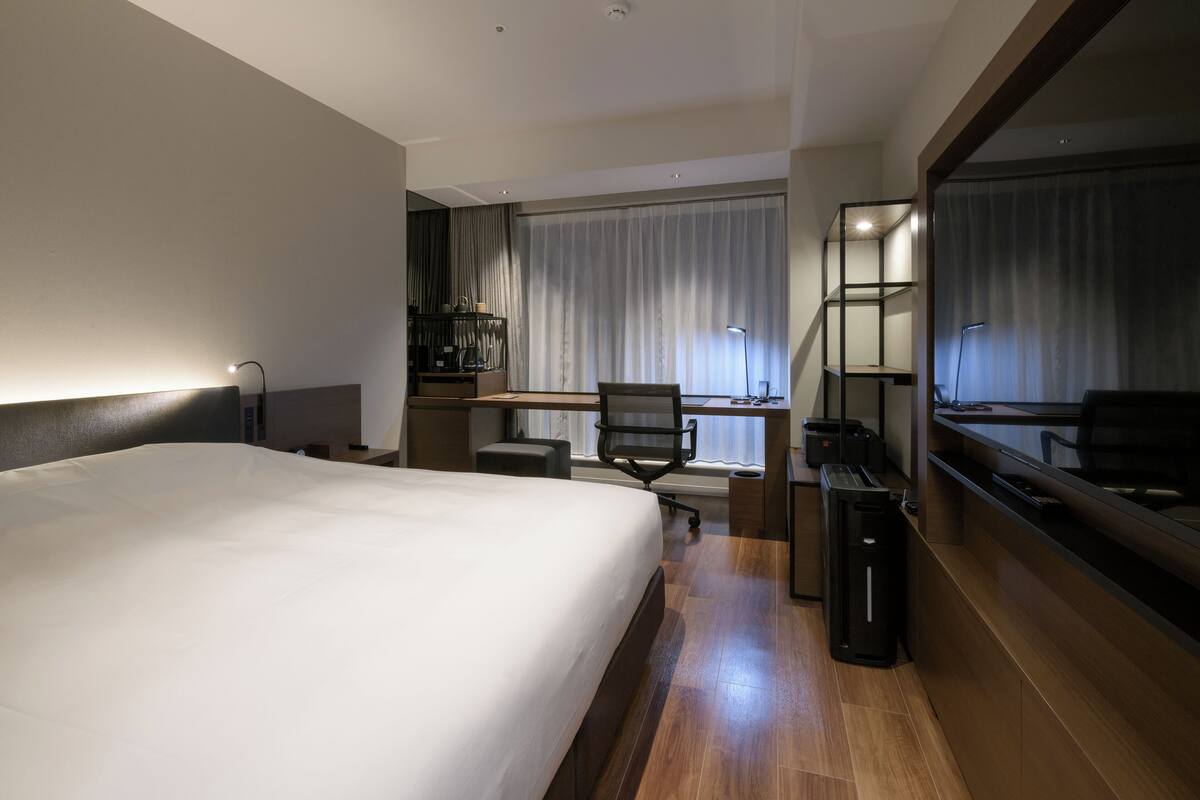 Une chambre d’hôtel avec un grand lit, un bureau avec une chaise, un ordinateur et une télévision.
