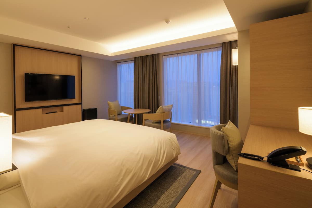 Une chambre d’hôtel dotée d’un grand lit, d’un téléviseur à écran plat fixé au mur, d’un bureau avec un téléphone et d’un coin salon avec des fauteuils et une table.