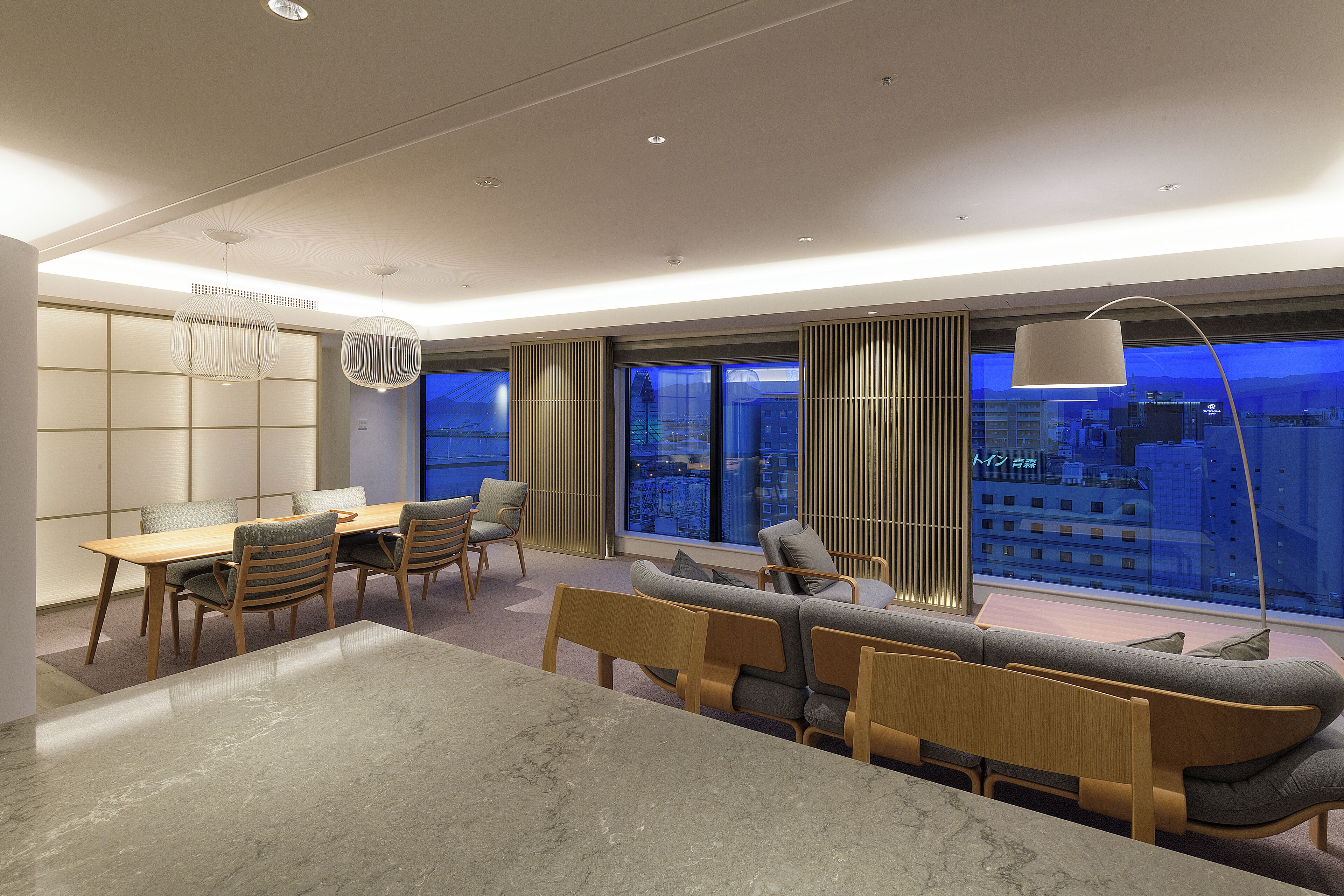 A modern interior with a dining area, seating, and a large window offering a city view.
