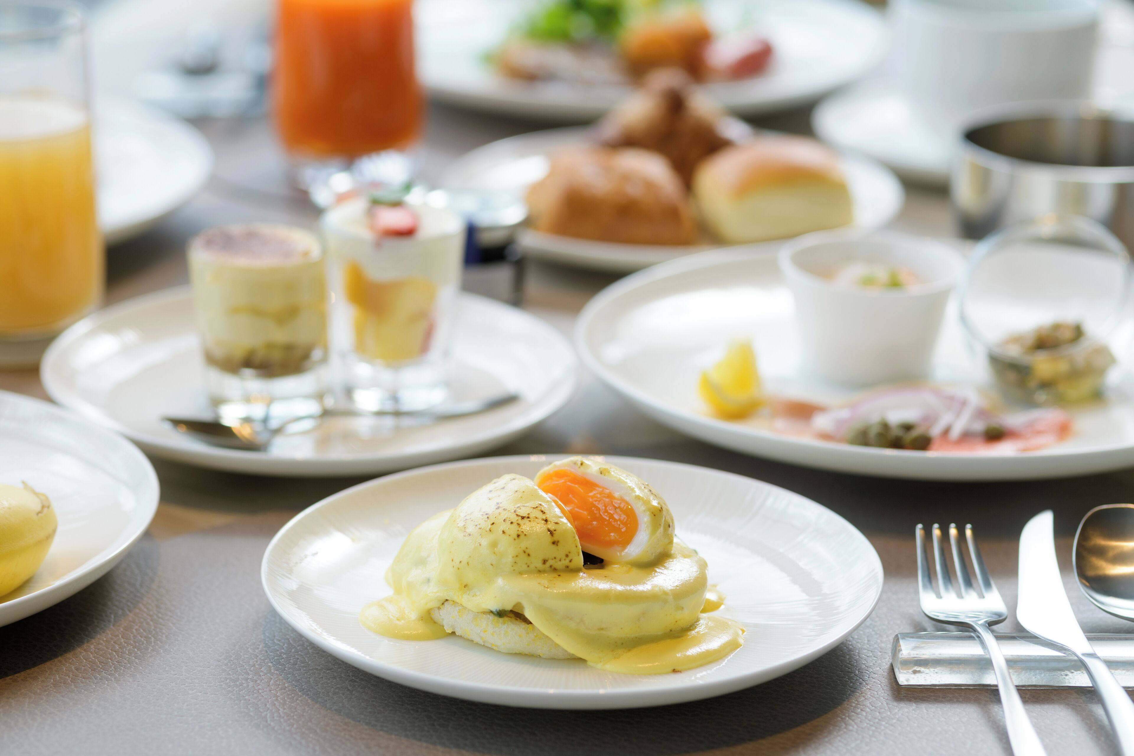 A breakfast setting with various dishes including eggs benedict, pastries, and a glass of orange juice.