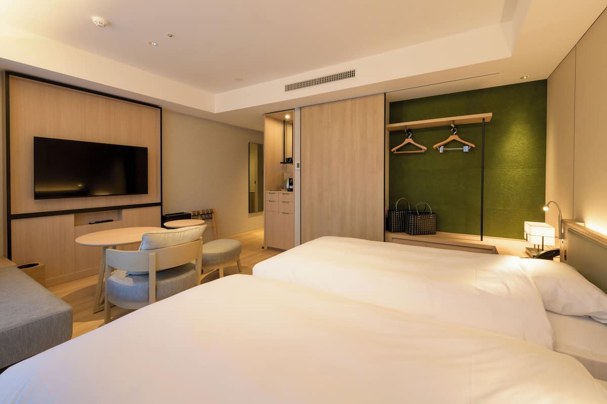Une chambre d’hôtel moderne dotée d’un grand lit, d’un bureau avec une chaise, d’un téléviseur à écran plat fixé au mur et d’une armoire avec un miroir.