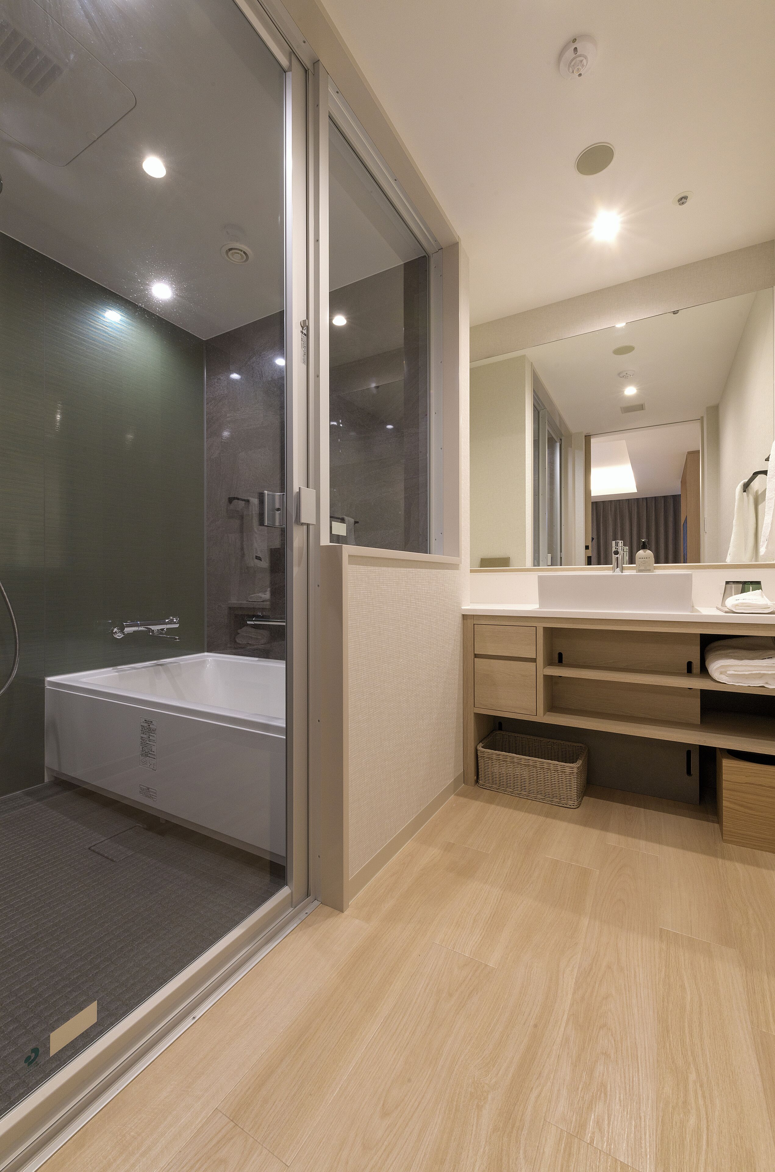 A modern bathroom with a glass shower enclosure, a bathtub, a vanity with a mirror, and a wooden floor.