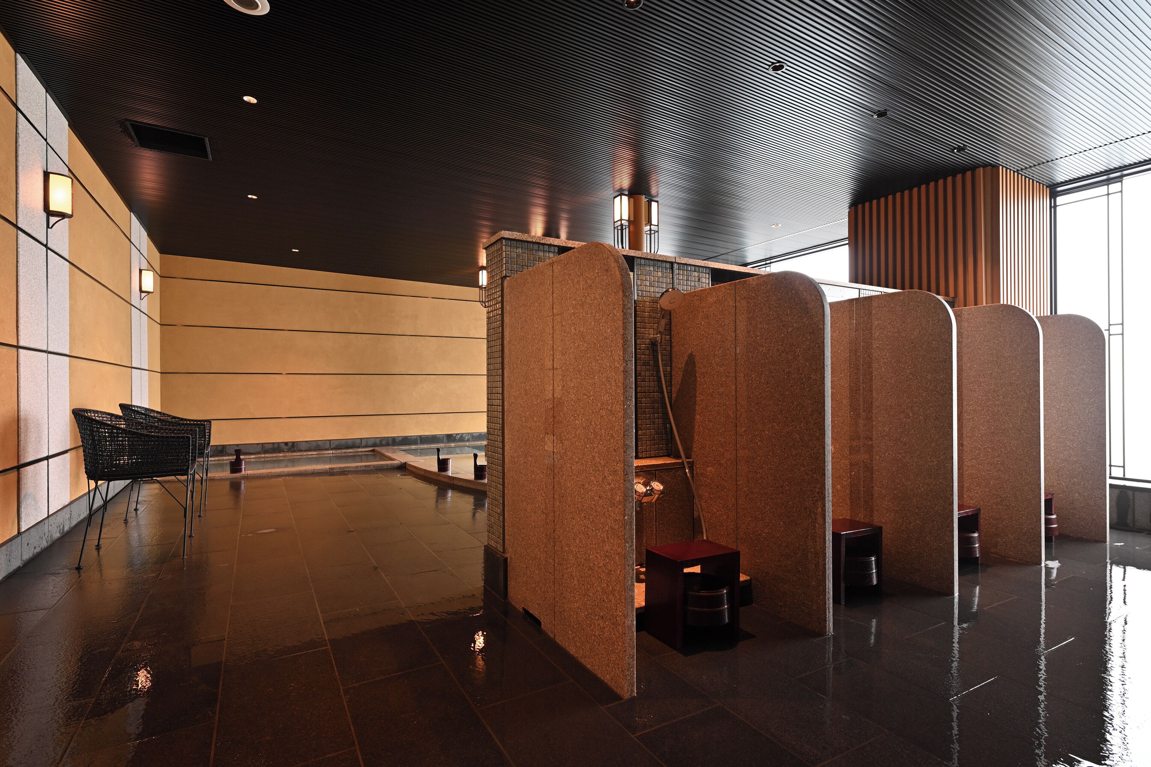 A modern restroom with a wet floor, a trash bin, and a seating area with chairs.