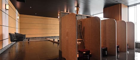 A modern restroom with a wet floor, a trash bin, and a seating area with chairs.