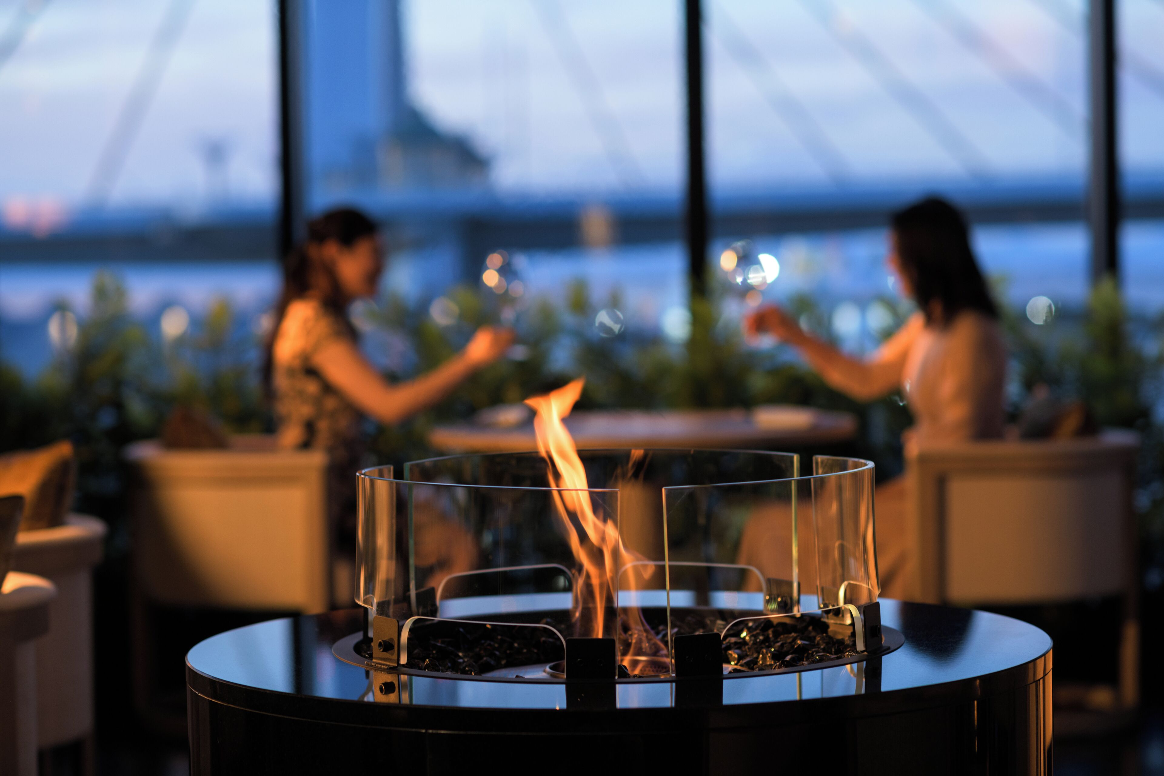 A modern outdoor seating area with a glass-top table and a built-in fire feature.