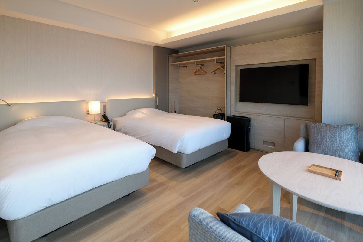 Une chambre d’hôtel moderne avec deux lits, un téléviseur fixé au mur et une petite table avec un plateau.