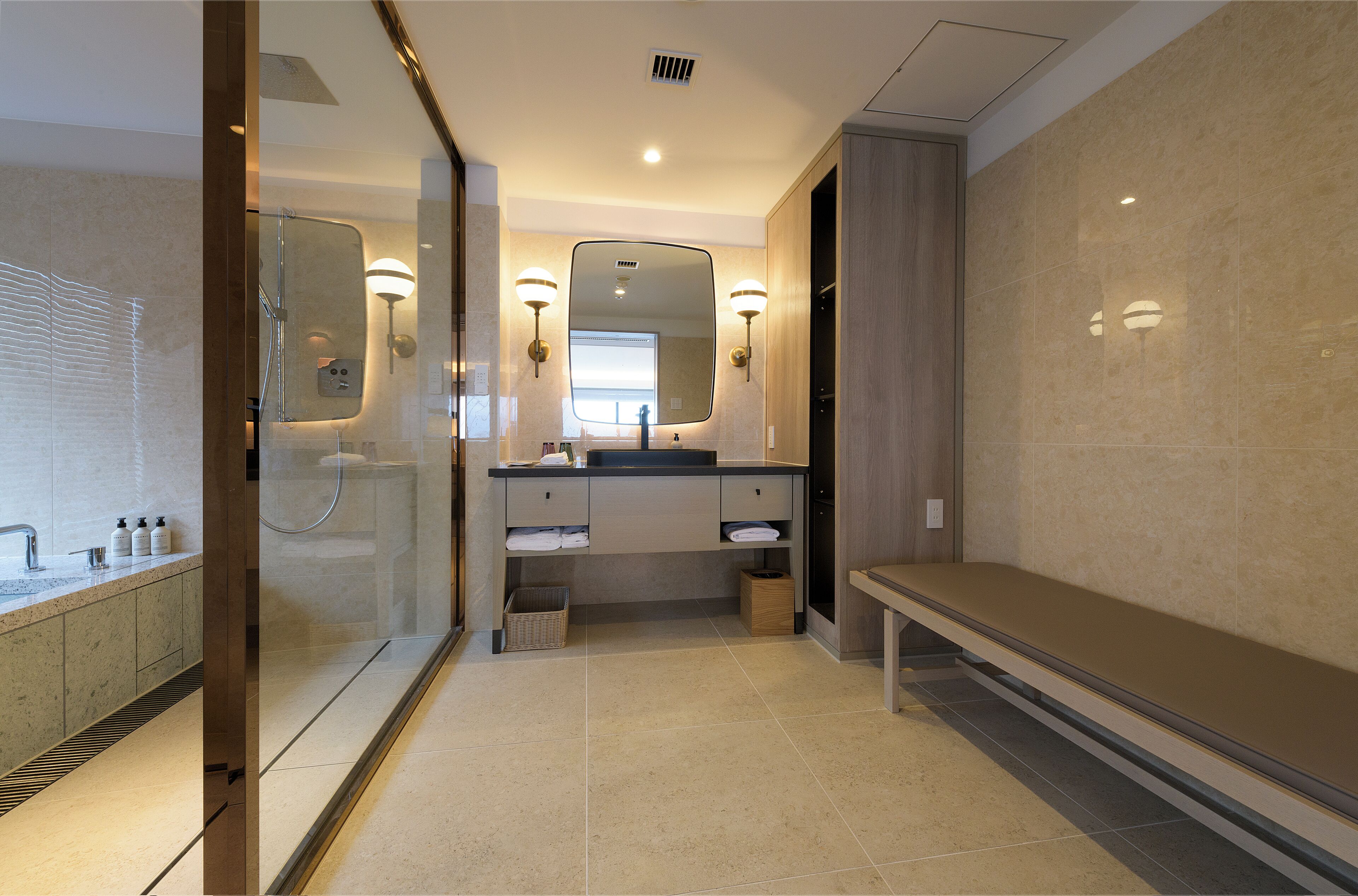 A modern bathroom with a glass-enclosed shower, a vanity with a mirror, and a bench.