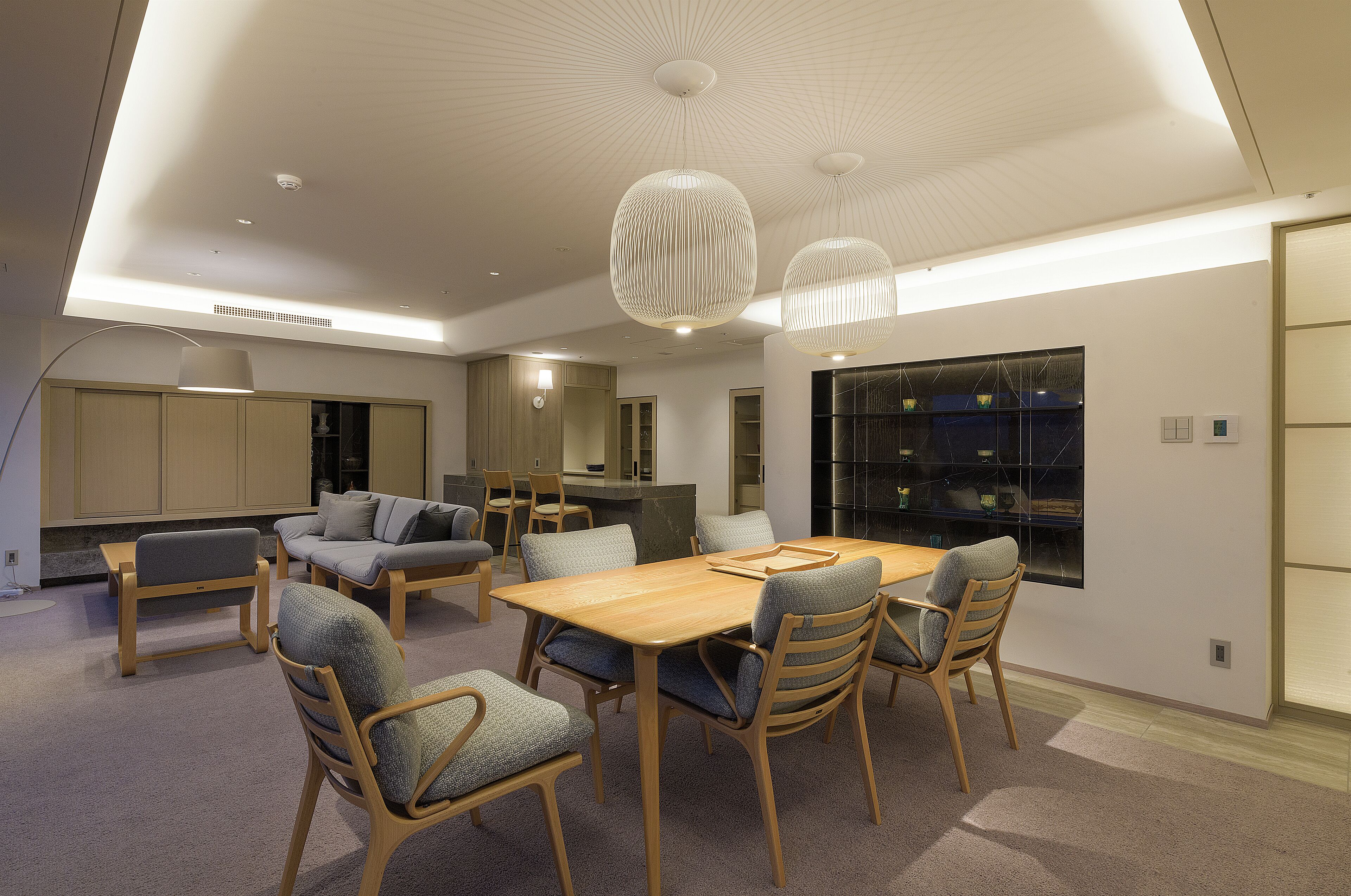 Uma sala de jantar moderna com mesa e cadeiras de madeira, um sofá e iluminação pendente.