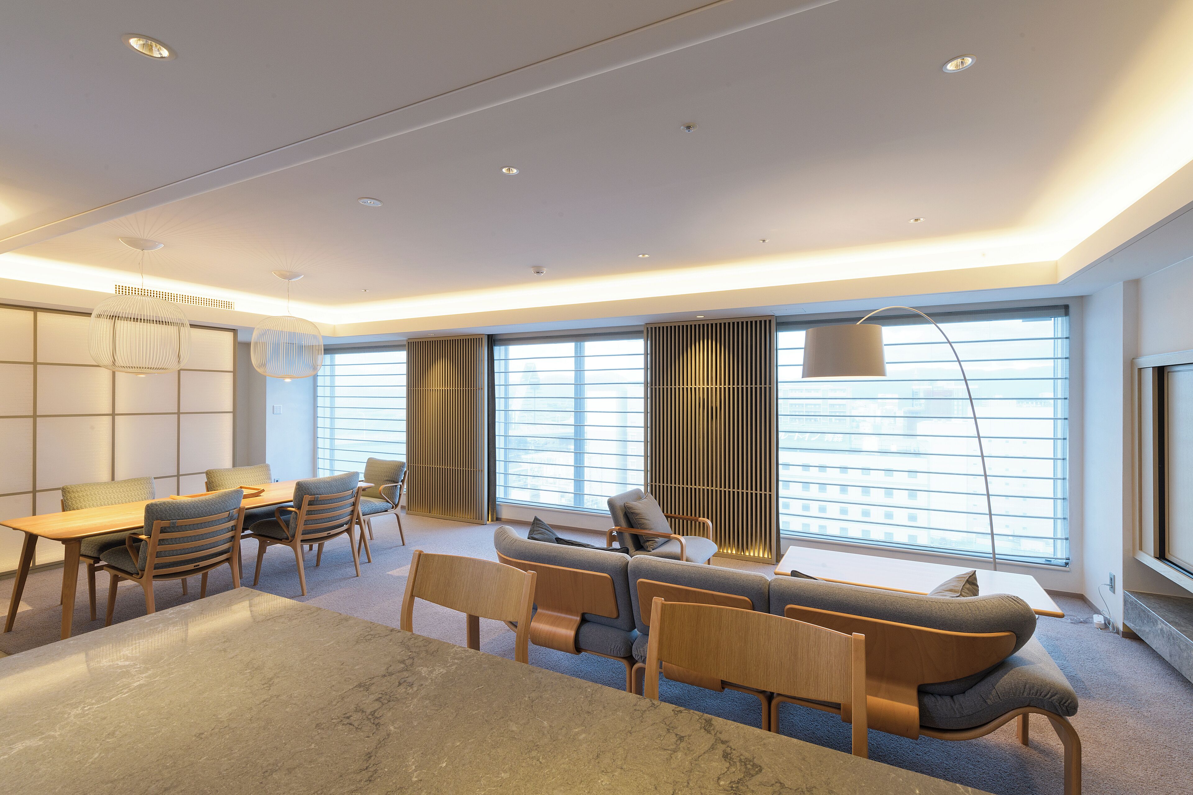 A modern living room with a sofa, chairs, a dining table, and a large window with blinds.
