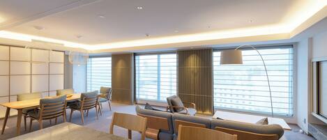 A modern living room with a sofa, chairs, a dining table, and a large window with blinds.