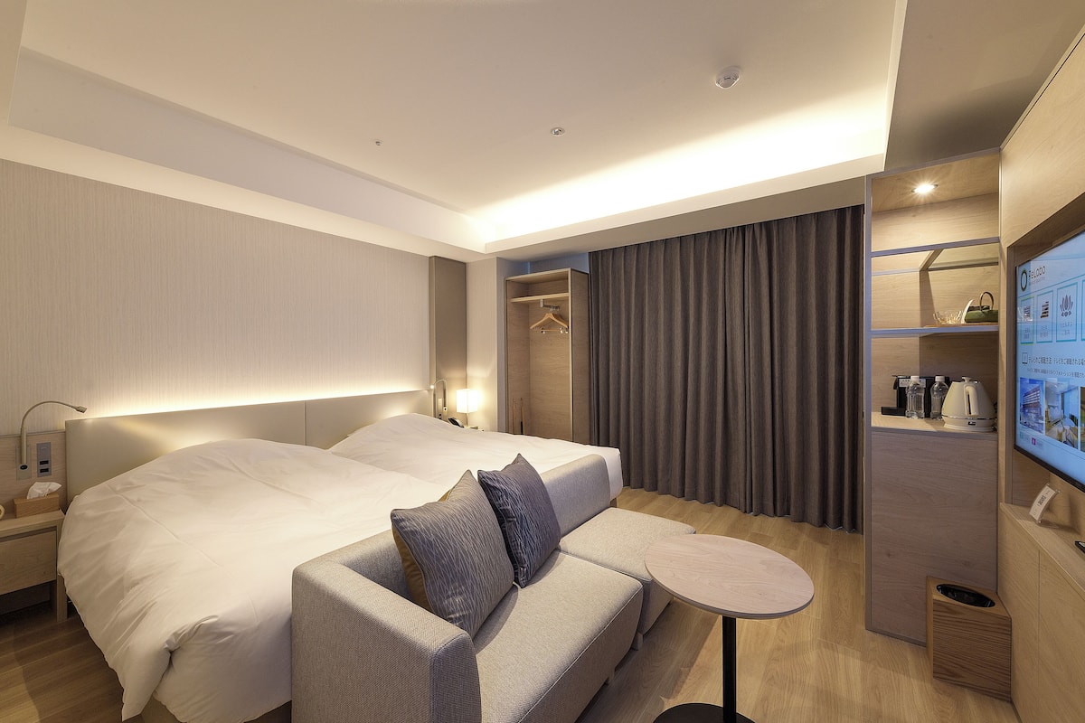 Une chambre d’hôtel avec deux lits, un canapé, une petite table, une télévision et une armoire.