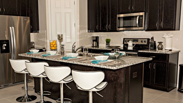 A modern kitchen with dark wood cabinets, stainless steel appliances, a granite countertop, and white bar stools. - Close to the Disney park! Family-sized house with Pool!!! (Kissimmee)