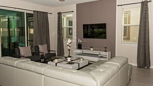 A modern living room with a white sofa, a coffee table, and a flat-screen TV mounted on the wall. - Close to the Disney park! Family-sized house with Pool!!! (Kissimmee)