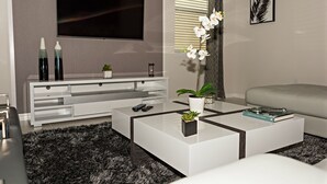 A modern living room with a flat-screen TV mounted on the wall, a white entertainment unit, a glass coffee table with a plant, and a grey sofa. - Close to the Disney park! Family-sized house with Pool!!! (Kissimmee)