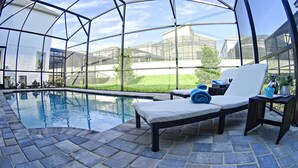 A covered outdoor swimming pool with lounge chairs and a small table with a potted plant. - Close to the Disney park! Family-sized house with Pool!!! (Kissimmee)