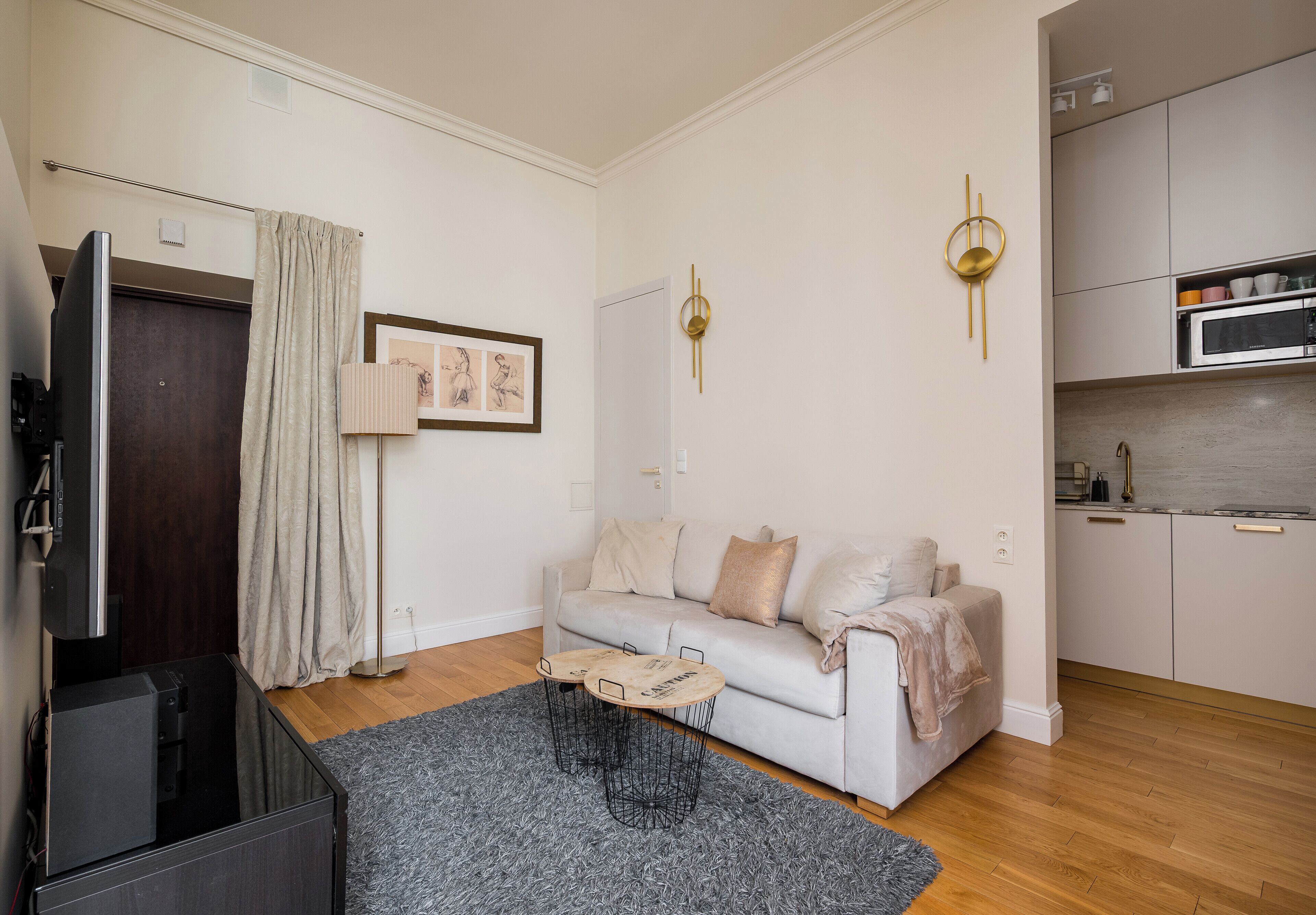 Ein modernes Wohnzimmer mit Sofa, Couchtisch, Flachbildfernseher und Küchenzeile inklusive Schränken und Mikrowelle.