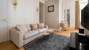 Un salon moderne avec un canapé, deux tables d’appoint, une horloge au mur et un téléviseur.