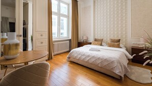 Une chambre à coucher avec un grand lit, une table de chevet, une chaise, une fenêtre avec des rideaux et une armoire.
