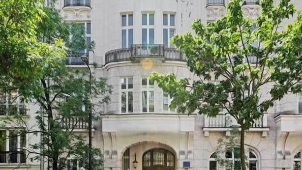 Un immeuble à plusieurs étages, de style architectural classique, doté d’une entrée centrale avec une grande porte en bois et de nombreuses fenêtres à chaque étage.
