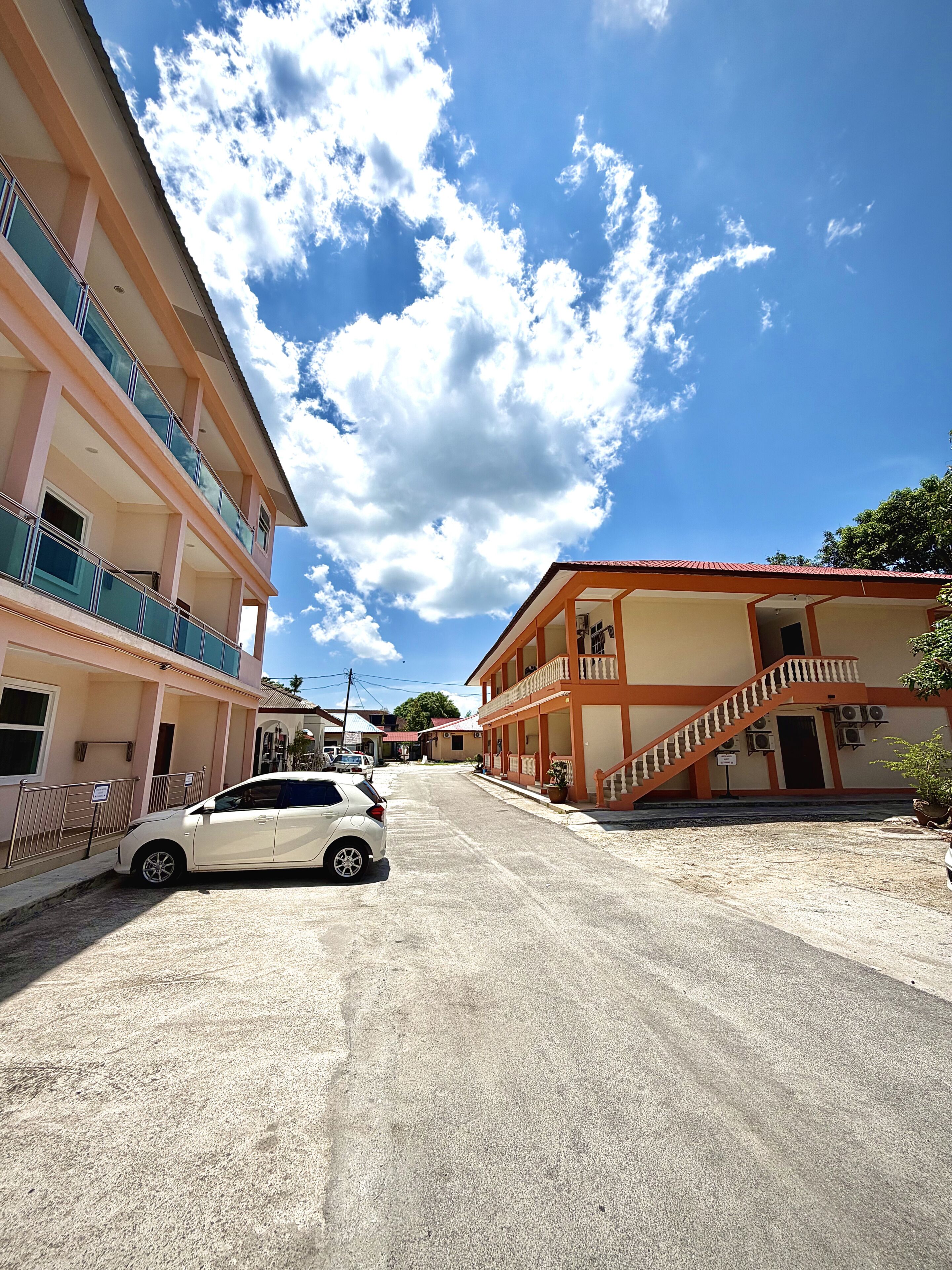 A multi-story building with balconies, a staircase, and a car parked in front.