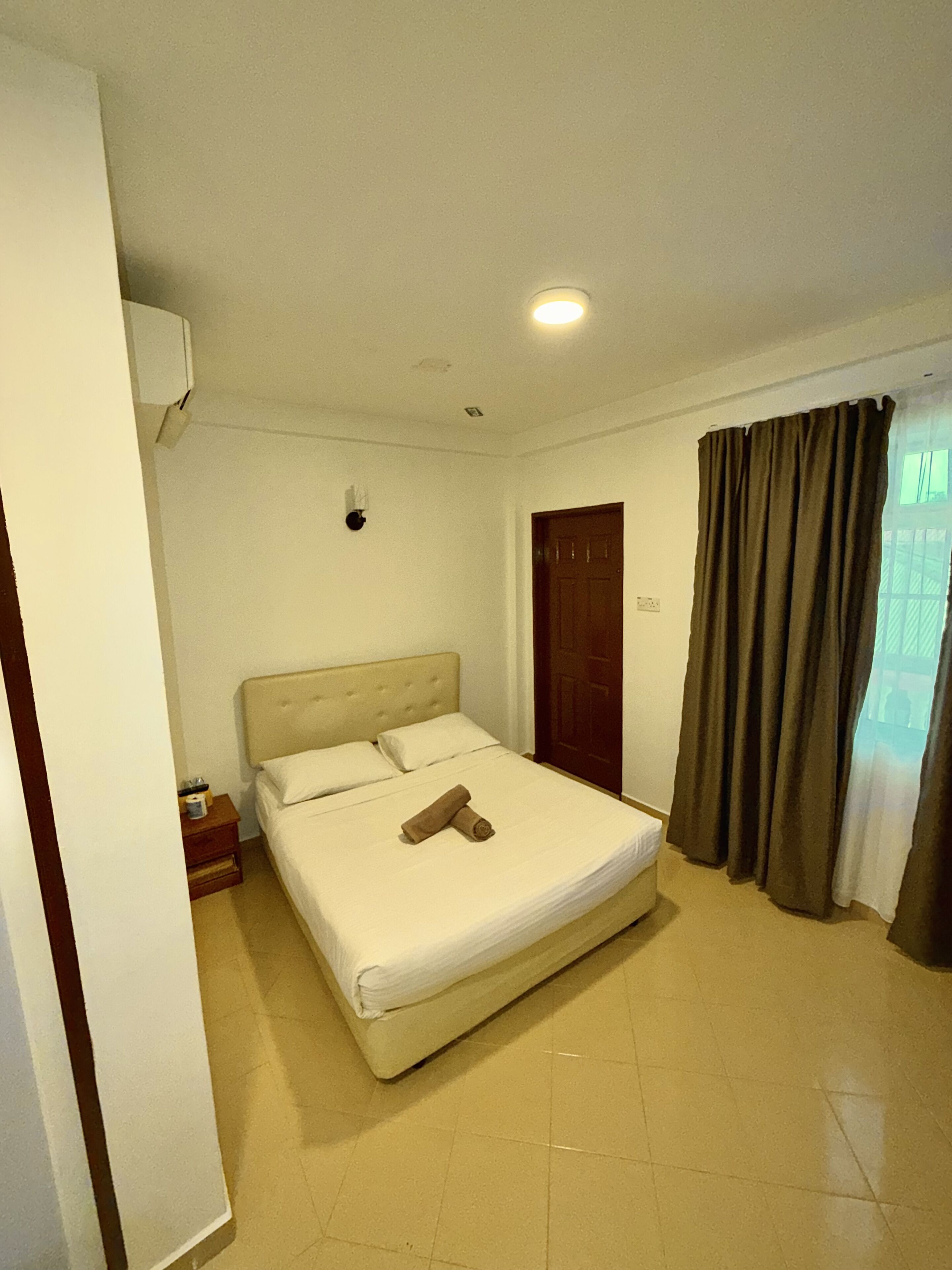 Habitación de hotel con cama, mesita de noche, una puerta y ventana con cortinas.