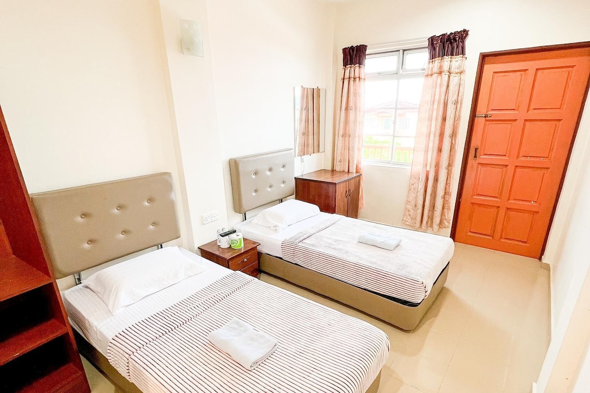 A hotel room with two beds, a wardrobe, a window with curtains, and a door.