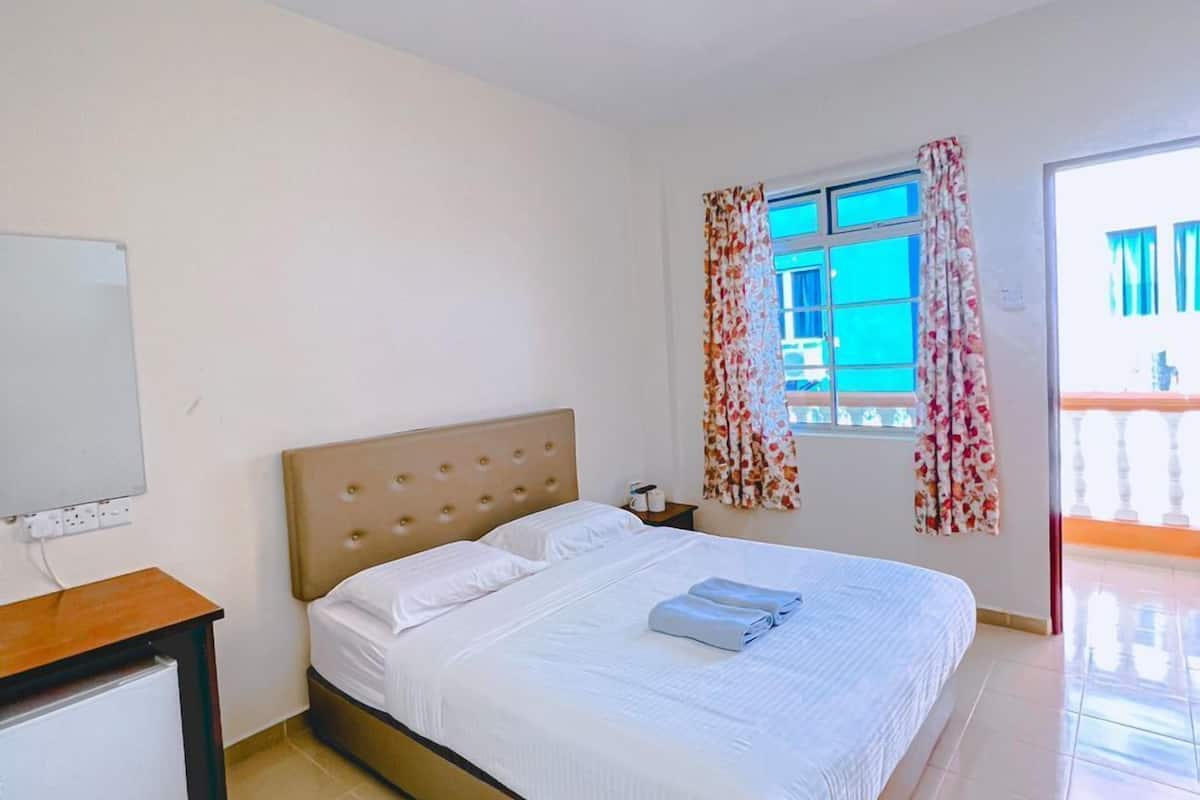 A bedroom with a bed, a bedside table, a TV, and a window with curtains.