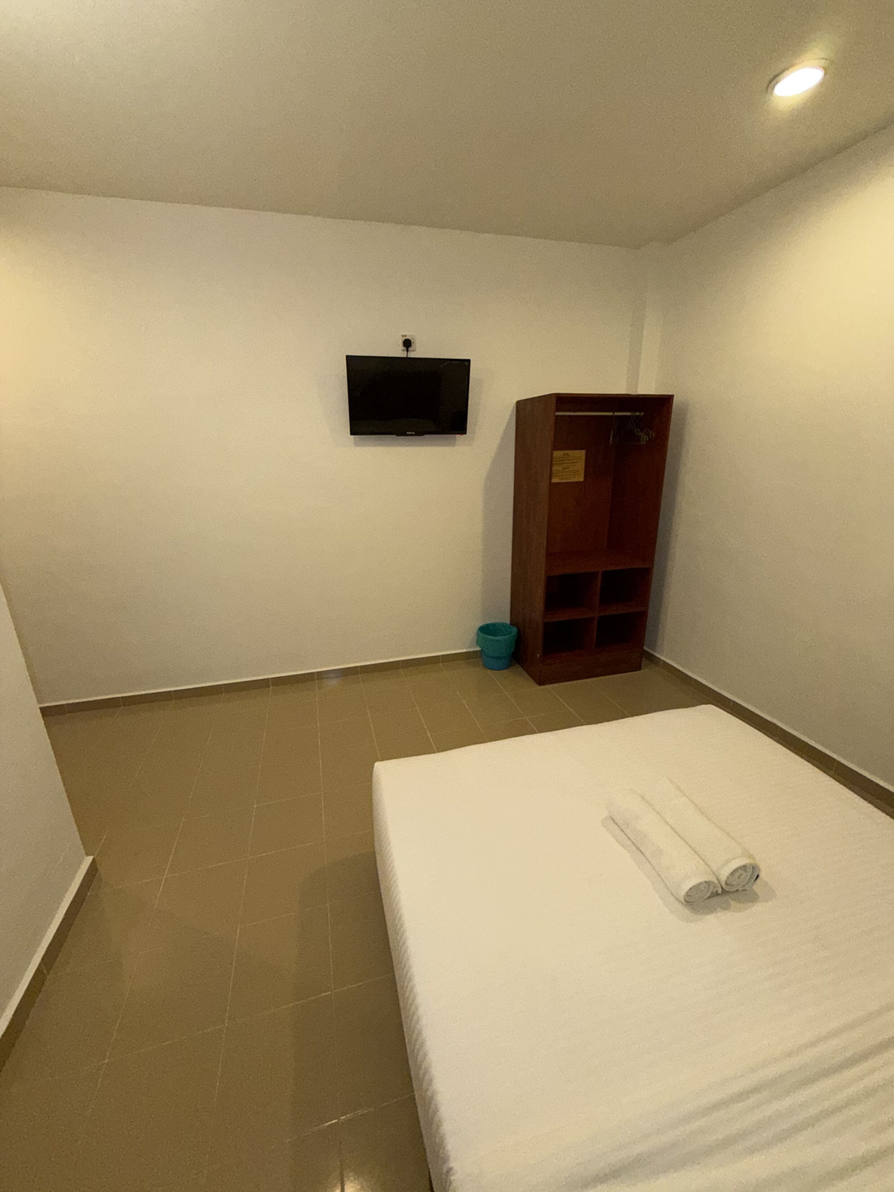 Une chambre d’hôtel avec un lit, un téléviseur fixé au mur, une armoire en bois et une poubelle.