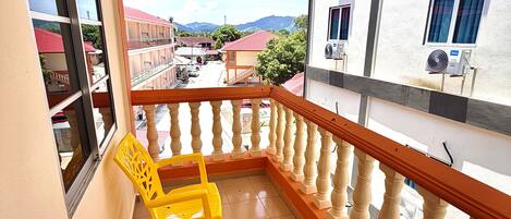 Un balcón con una silla amarilla, barandilla y vistas a edificios y montañas.