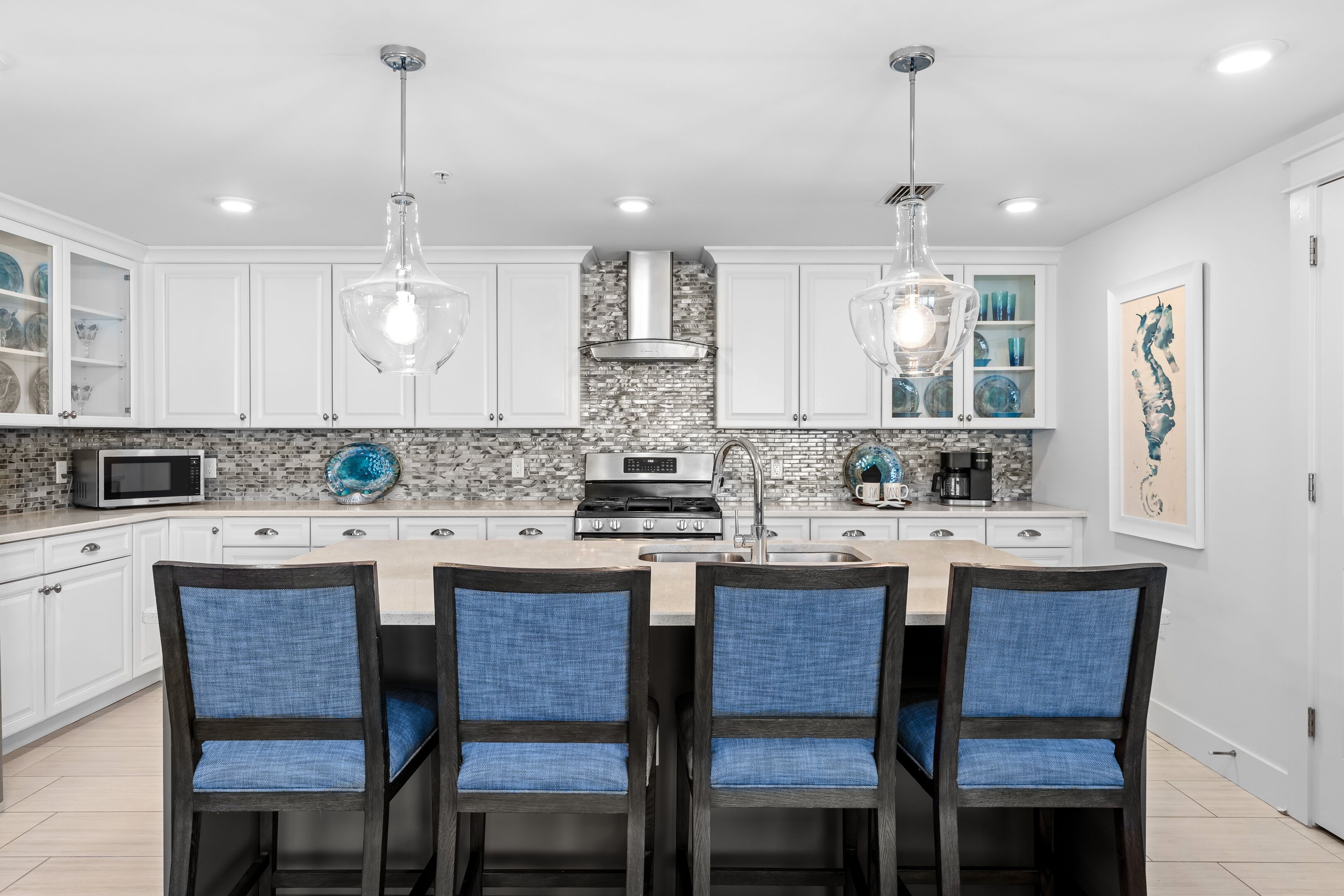 A kitchen with white cabinets, a central island with bar stools, a microwave, and a stove.