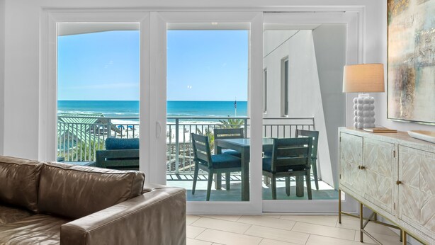 A room with a sliding glass door leading to a balcony with a view of the ocean. There is a beige sofa and a cabinet with a lamp. - Blu 300 ~ Stunning 4BR w/ Gulf Views ~ Free Beach Service (Fort Walton Beach)
