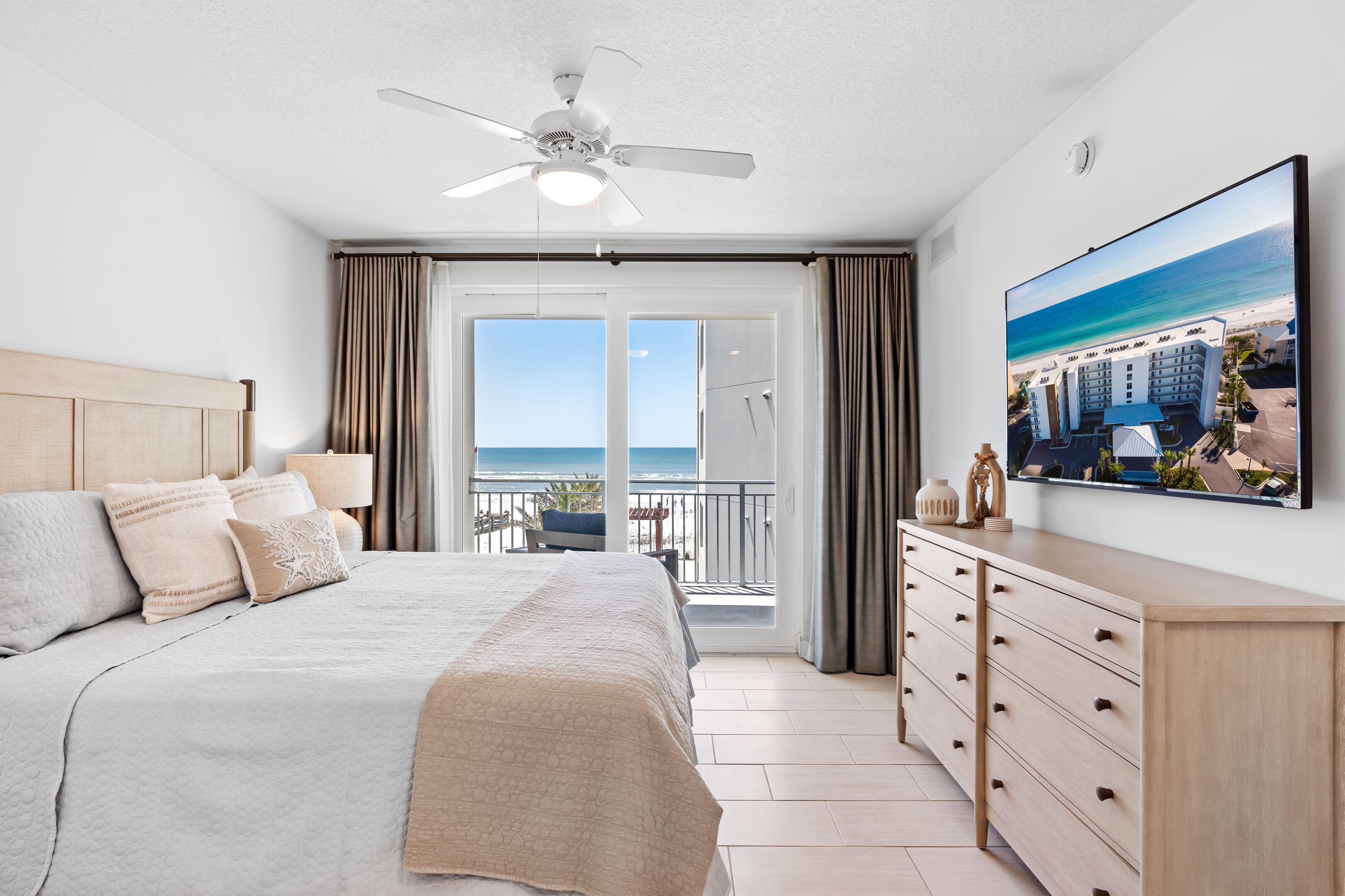 Une chambre d’hôtel dotée d’un grand lit, d’un ventilateur de plafond, d’un balcon avec vue sur l’océan et d’un téléviseur à écran plat fixé au mur.