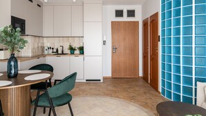 A modern kitchen with white cabinets, a wooden door, and a blue tiled wall. - Saska Kępa Cosy Studio (Warszawa)