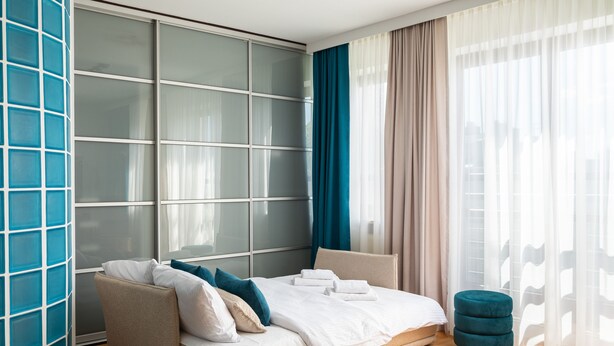 A modern hotel room with a sofa bed, a small ottoman, and a large window with curtains. - Saska Kępa Cosy Studio (Warszawa)