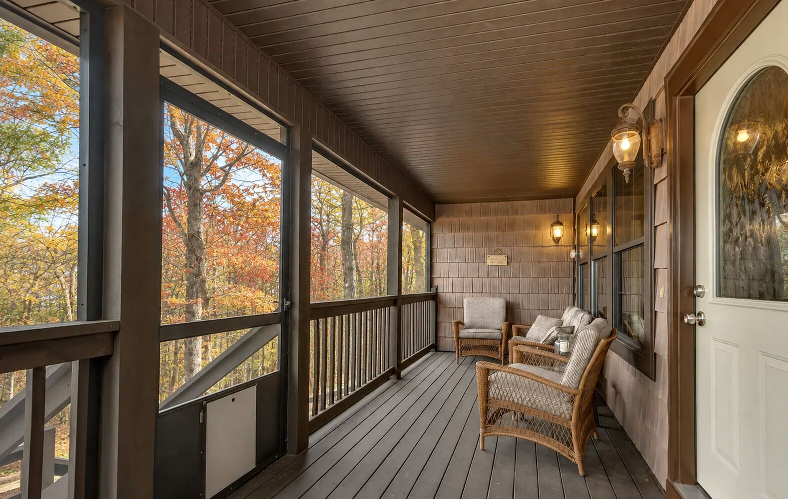 A covered porch with a wooden floor, two wicker chairs, and a white door with a glass panel.