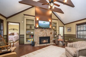 A living room with a stone fireplace, a television mounted above it, and a ceiling fan.