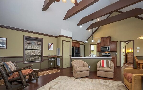 A spacious living room with a large window, a fireplace, and a kitchen area with wooden cabinets and a central island.
