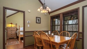 Een eetkamer met een houten tafel en stoelen, een kroonluchter en een raam met uitzicht op bomen.